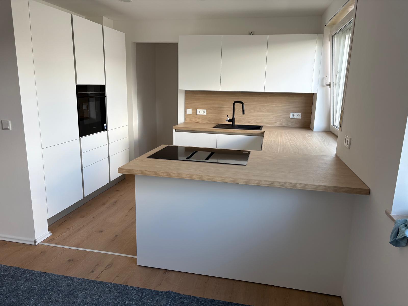 Grifflose weiße U-Küche mit Holzoptik-Arbeitsplatte, Kochfeld in der Theke und deckenhoher Hochschrankzeile
